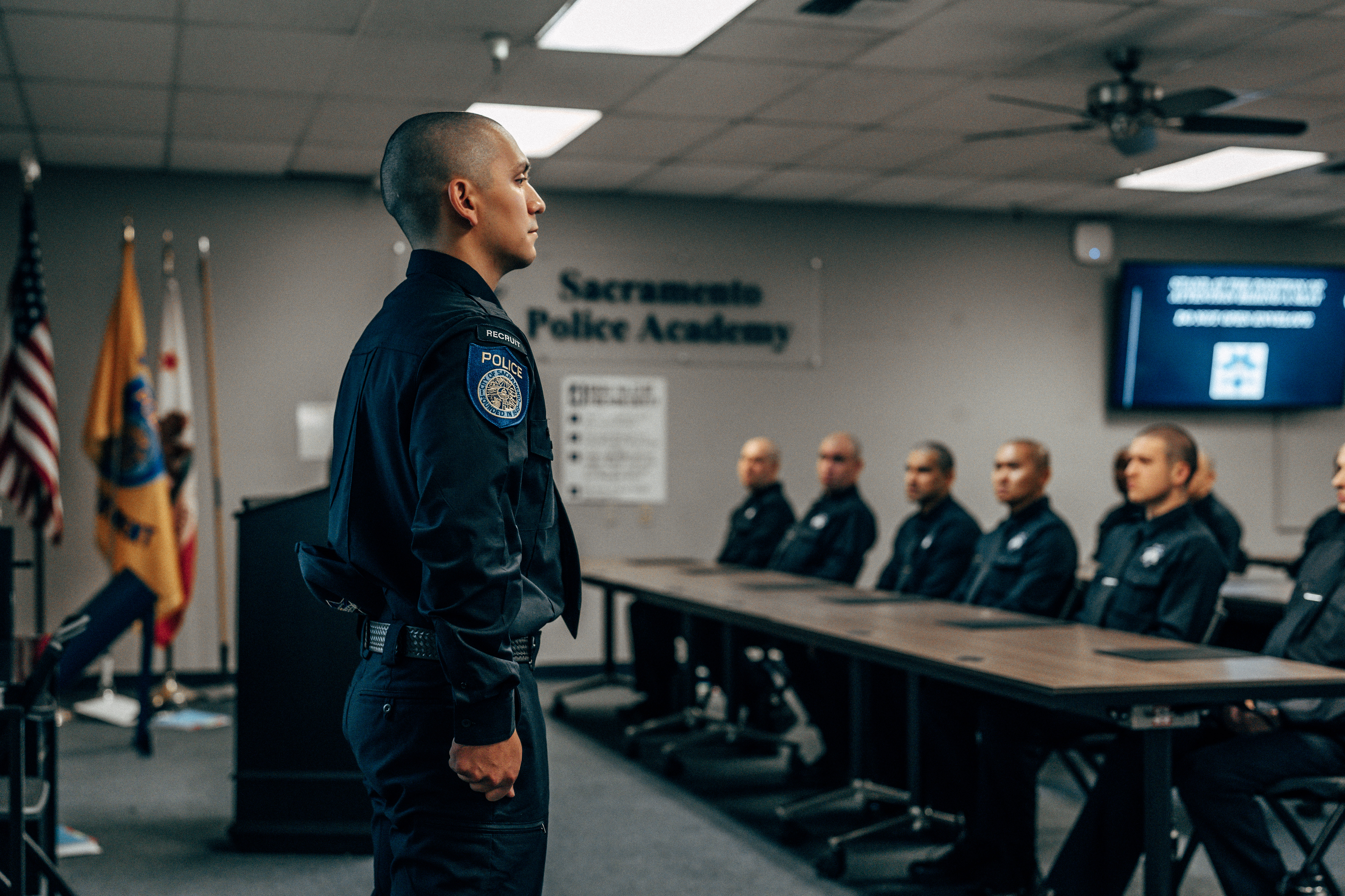 A photo of a Sacramento Police Department police officer recruit standing at attention in a classroom