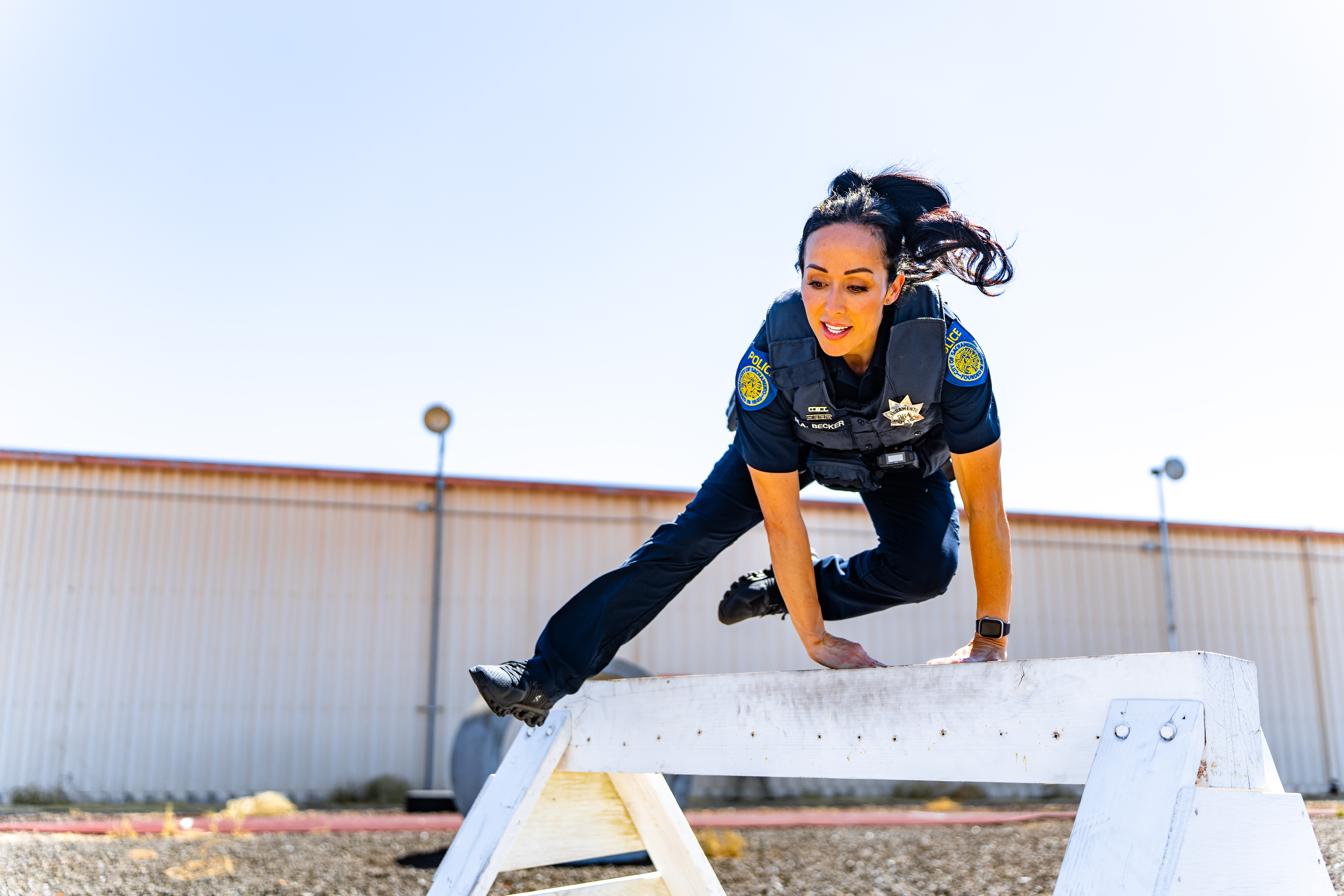 This is a photo of a female officer in full uniform jumping over an obstacle outdoors